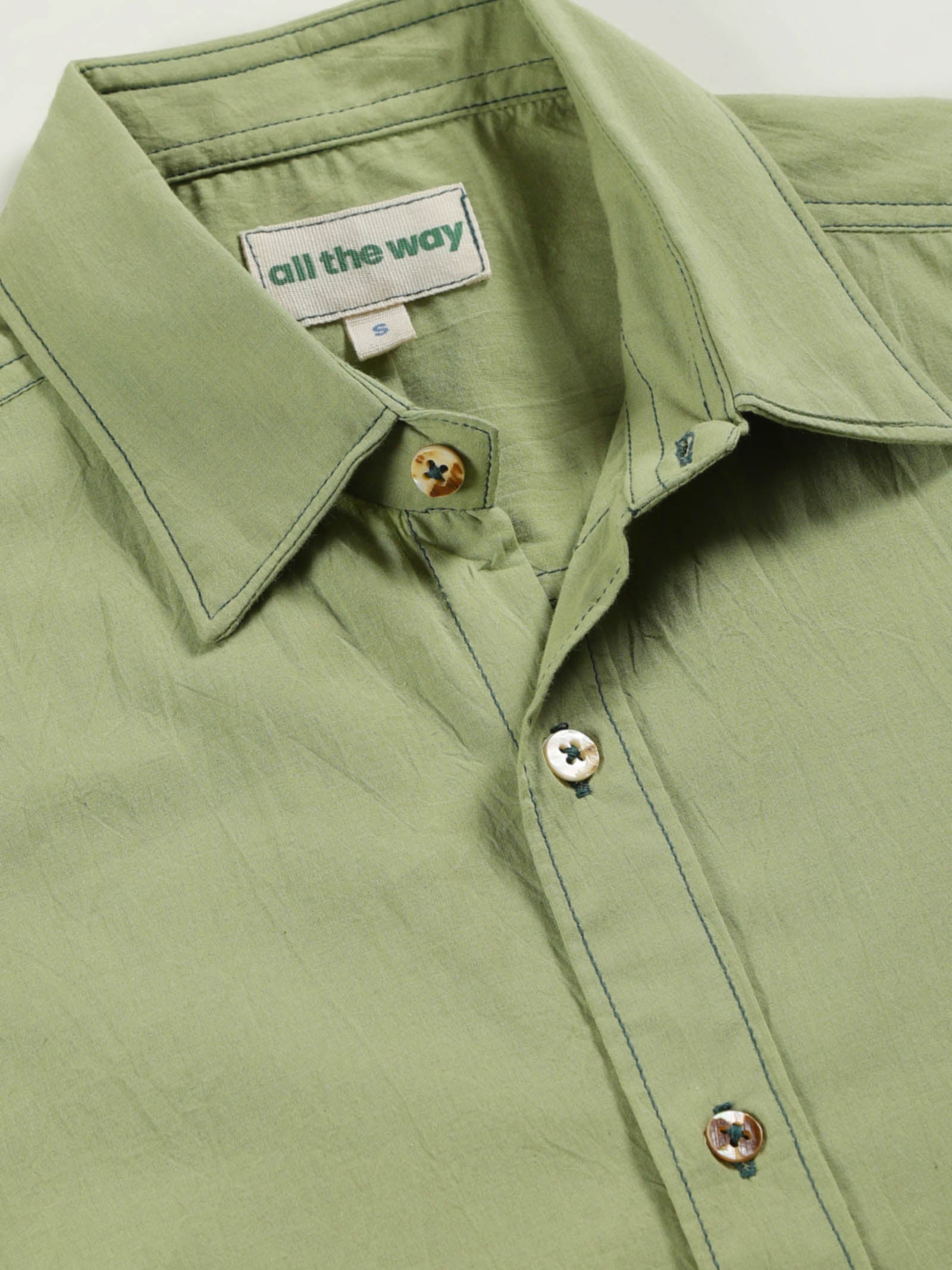 Close-up of pale olive plant-dyed organic cotton shirt with natural shell buttons and organic cotton label printed in water-based ink, along with contrast stitching.