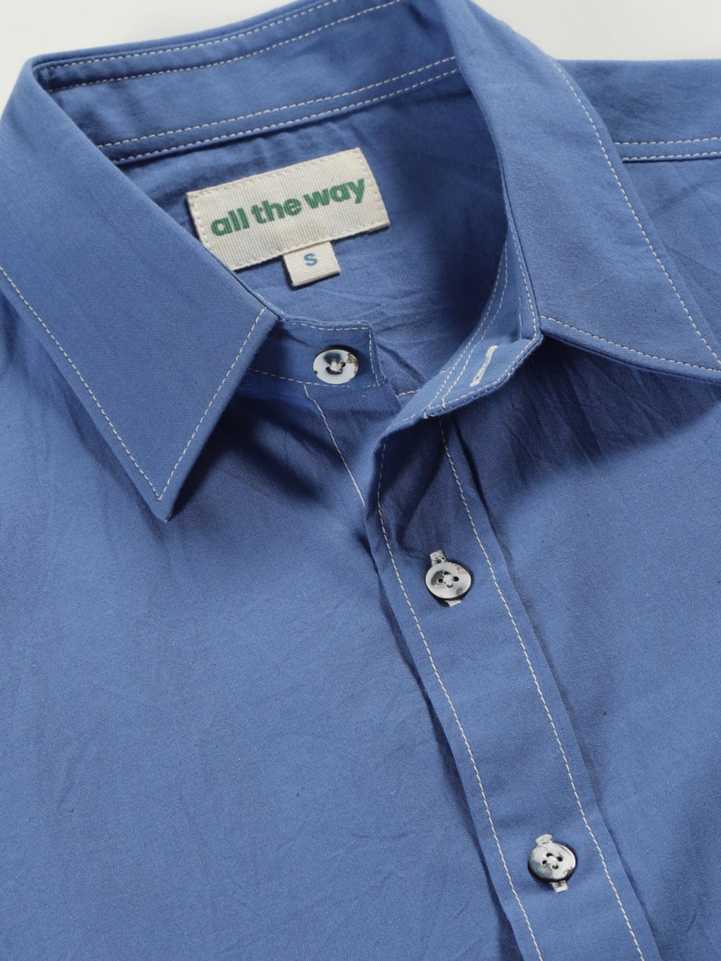 Close-up of quiet blue organic cotton shirt with organic cotton label printed in water-based ink, natural wooden buttons and contrast threads.
