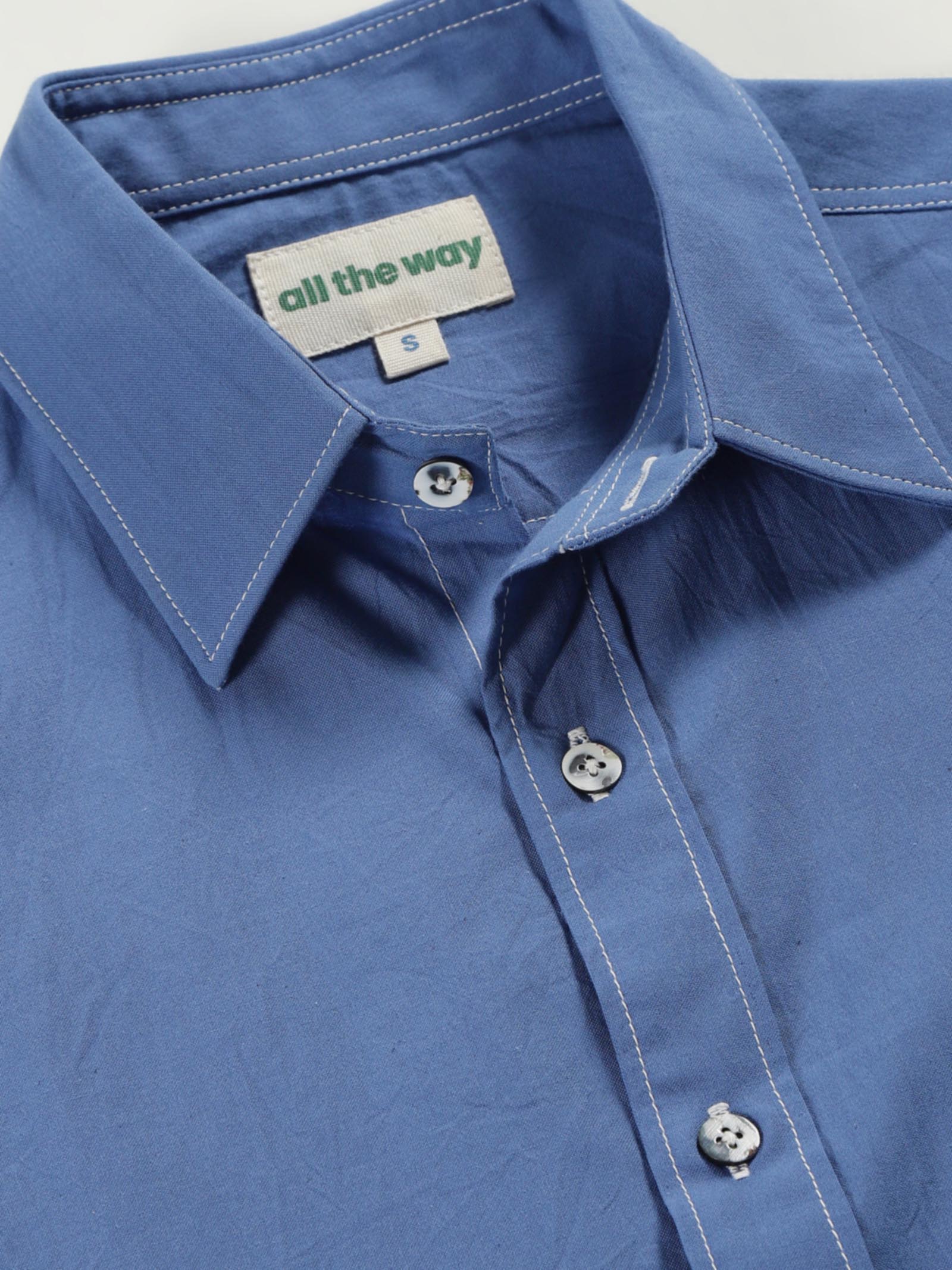 Close-up of quiet blue organic cotton shirt with organic cotton label printed in water-based ink, natural wooden buttons and contrast threads.