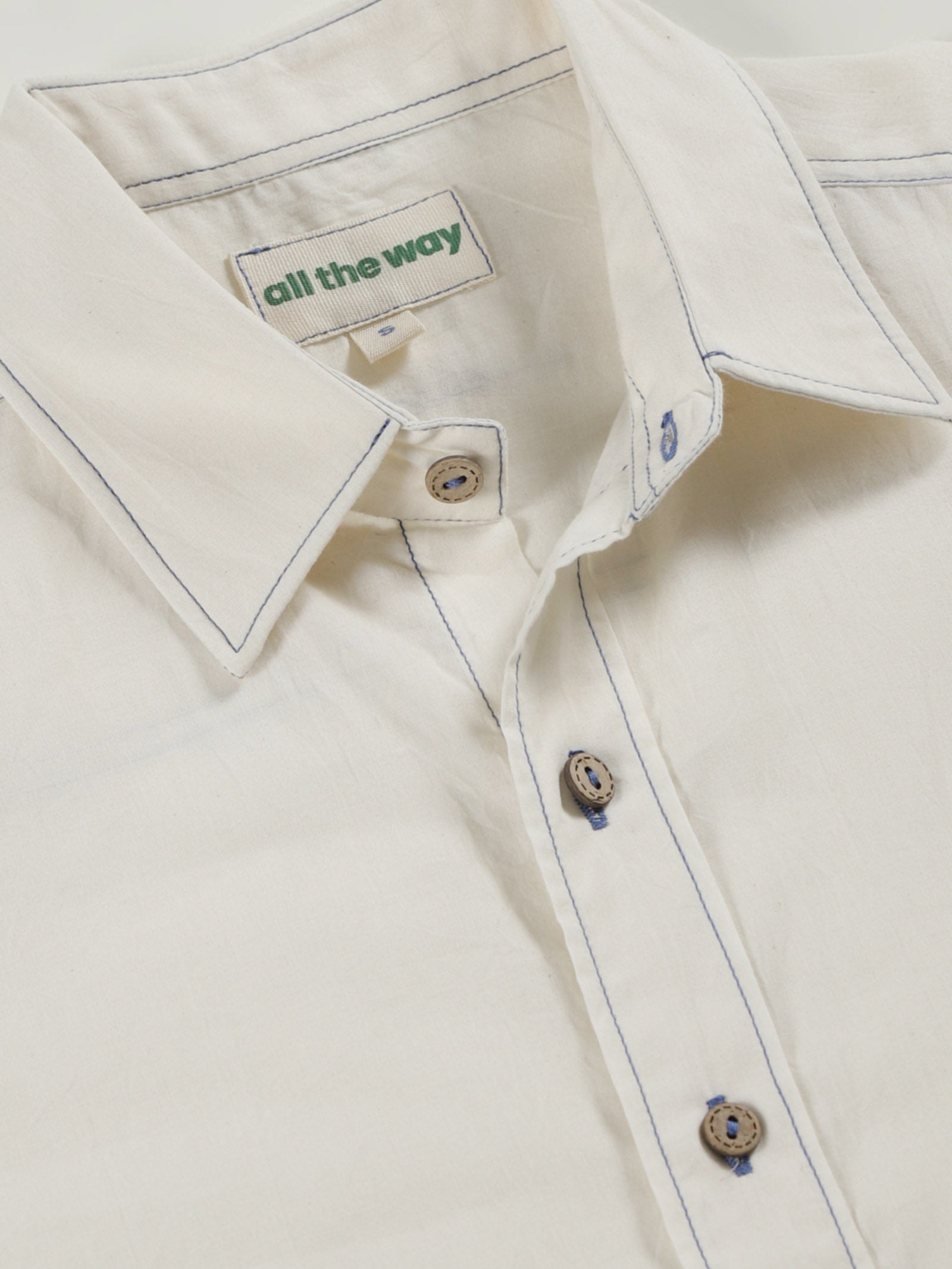 Close-up of undyed organic cotton shirt with organic cotton label printed in water-based ink, natural wooden buttons and contrast threads.