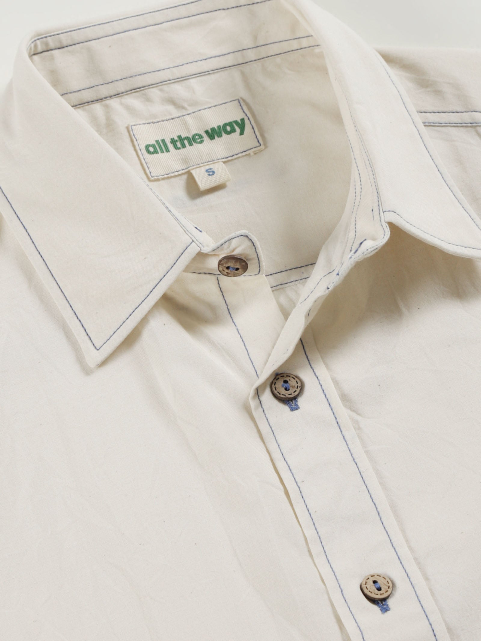 Close-up of pale undyed organic cotton shirt with organic cotton label printed in water-based ink, natural wooden buttons and contrast threads.