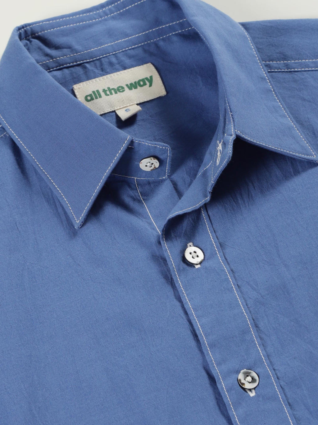 Close-up of pale olive plant-dyed organic cotton shirt with organic cotton label printed in water-based ink, natural shell buttons, and contrast cotton threads.