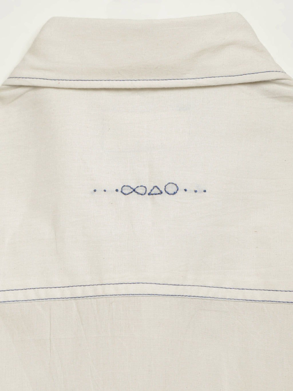 Hand-embroidered symbols on the back yoke of an organic cotton shirt — infinity, triangle and circle motifs in white thread, handcrafted by artisans in Tamil Nadu