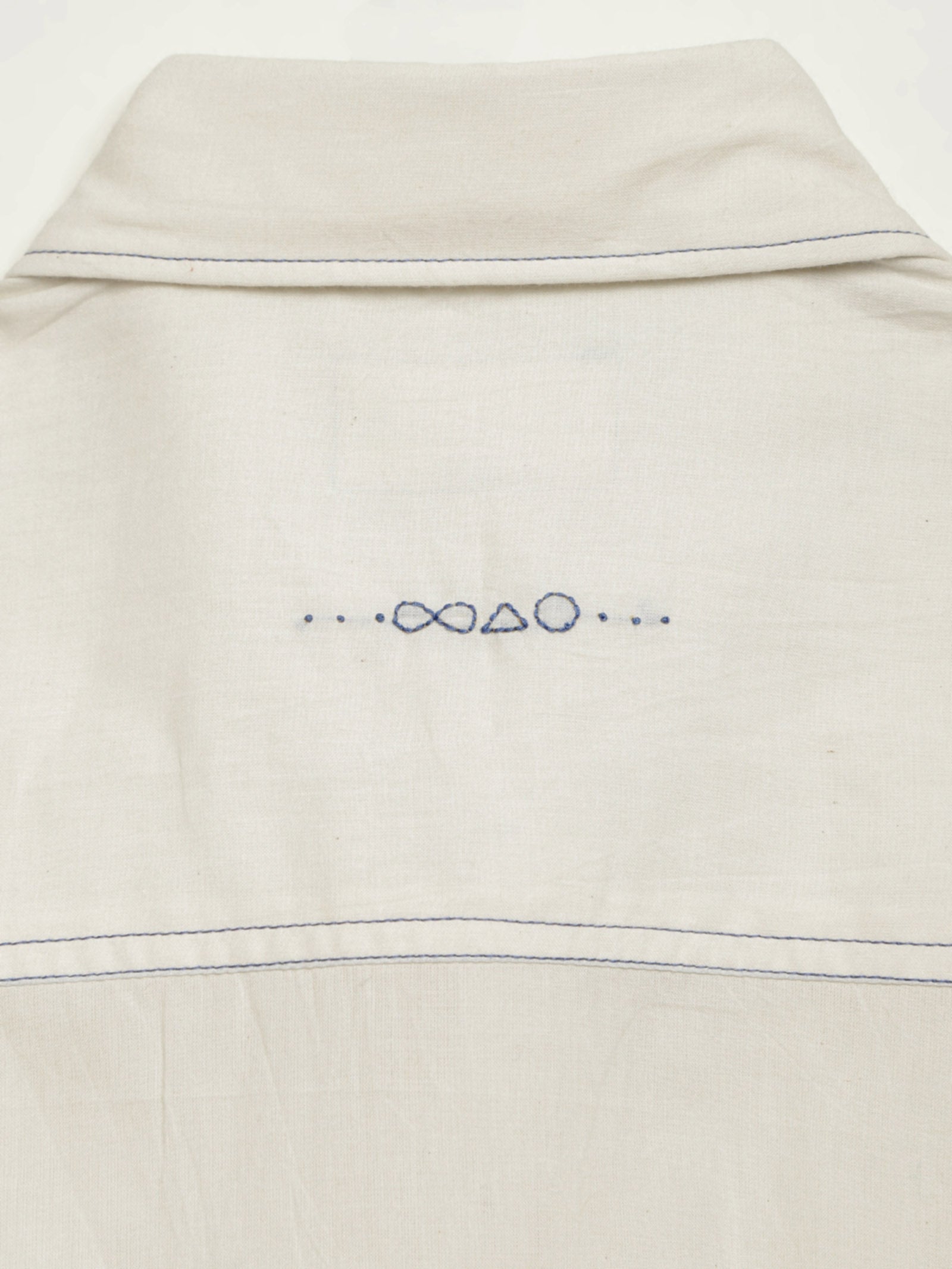 Hand-embroidered symbols on the back yoke of an organic cotton shirt — infinity, triangle and circle motifs in white thread, handcrafted by artisans in Tamil Nadu