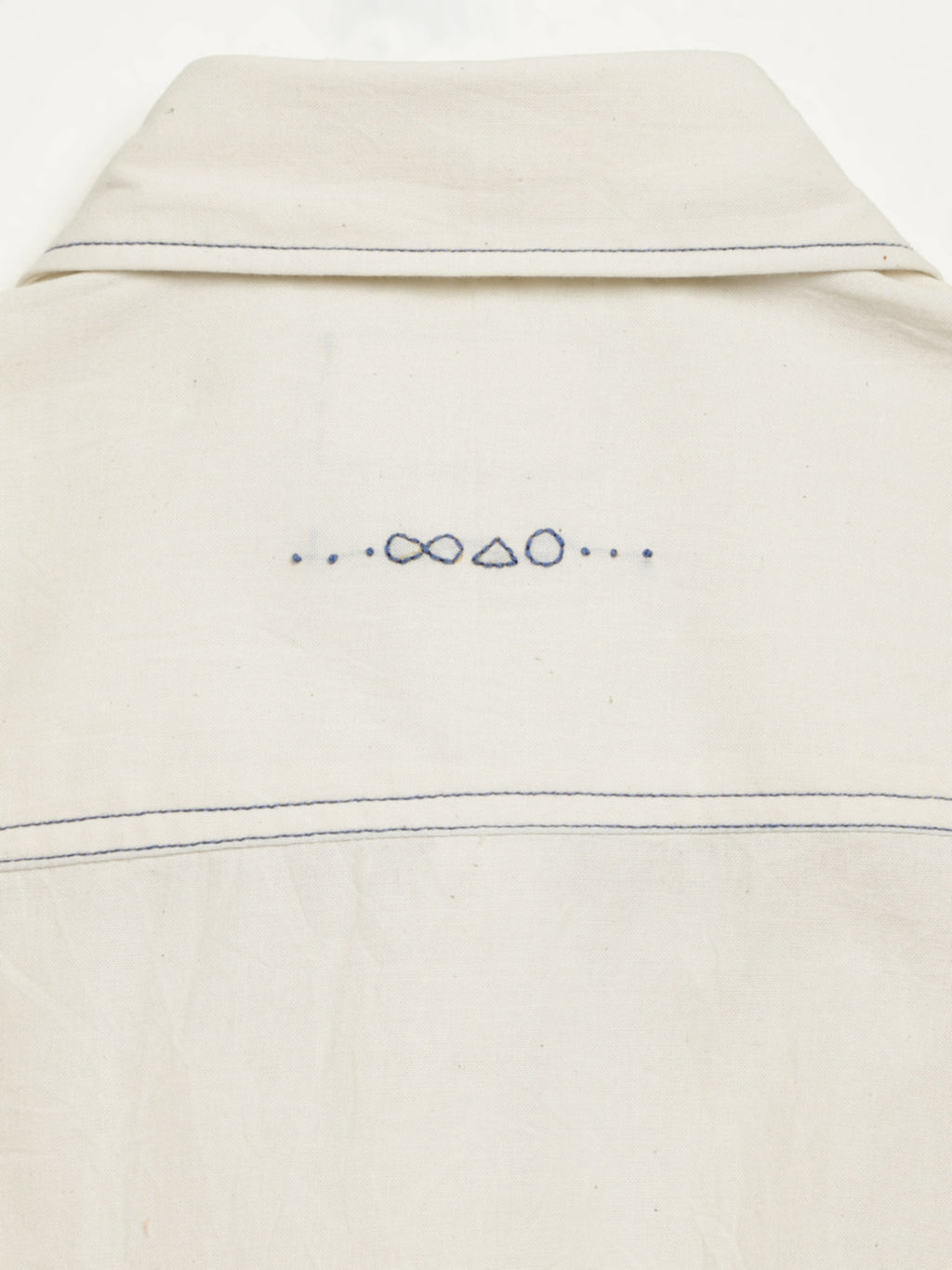 Hand-embroidered symbols on the back yoke of an organic cotton shirt — infinity, triangle and circle motifs in white thread, handcrafted by artisans in Tamil Nadu
