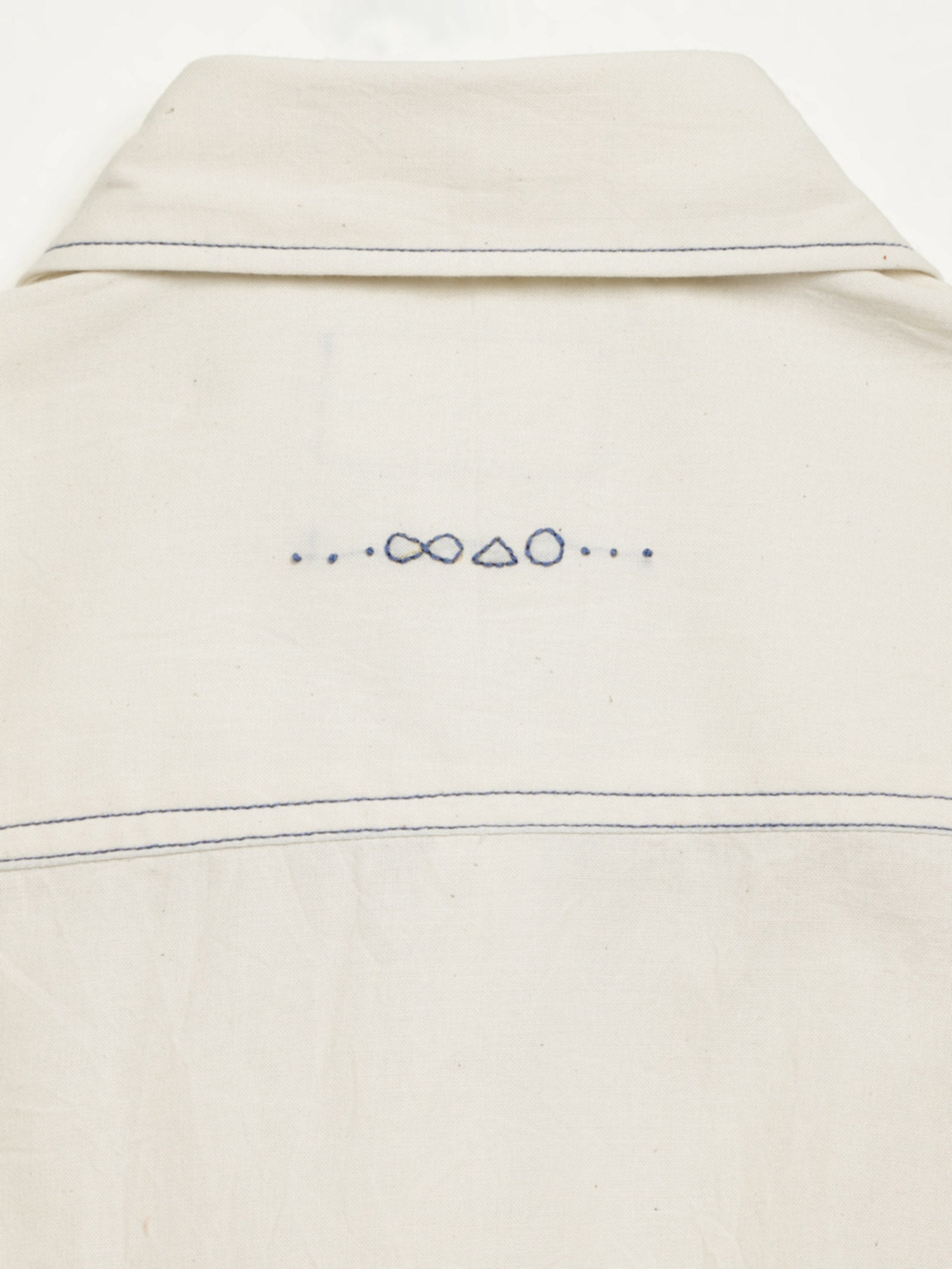 Hand-embroidered symbols on the back yoke of an organic cotton shirt — infinity, triangle and circle motifs in white thread, handcrafted by artisans in Tamil Nadu