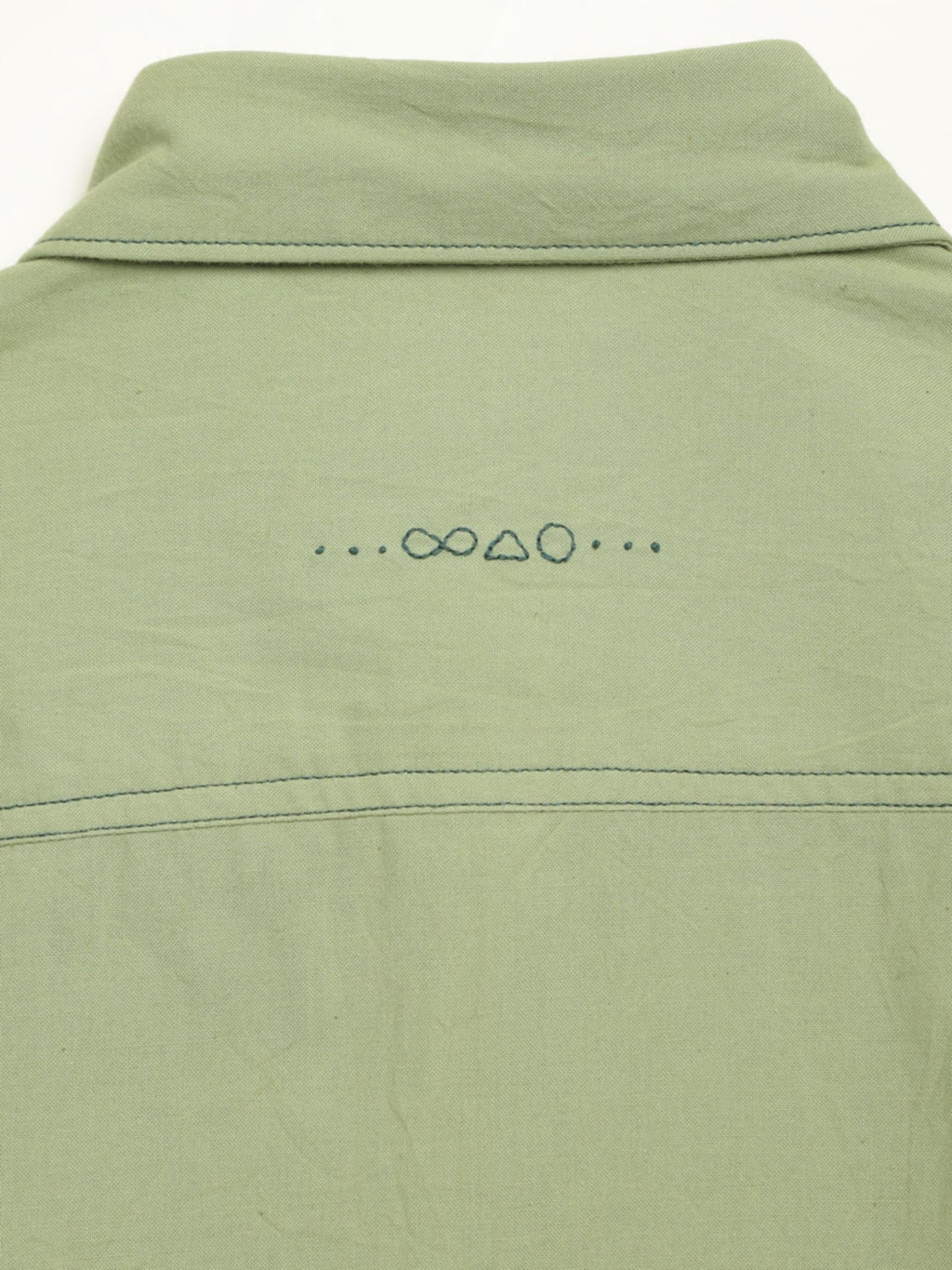 Hand-embroidered symbols on the back yoke of an organic cotton shirt — infinity, triangle and circle motifs in white thread, handcrafted by artisans in Tamil Nadu