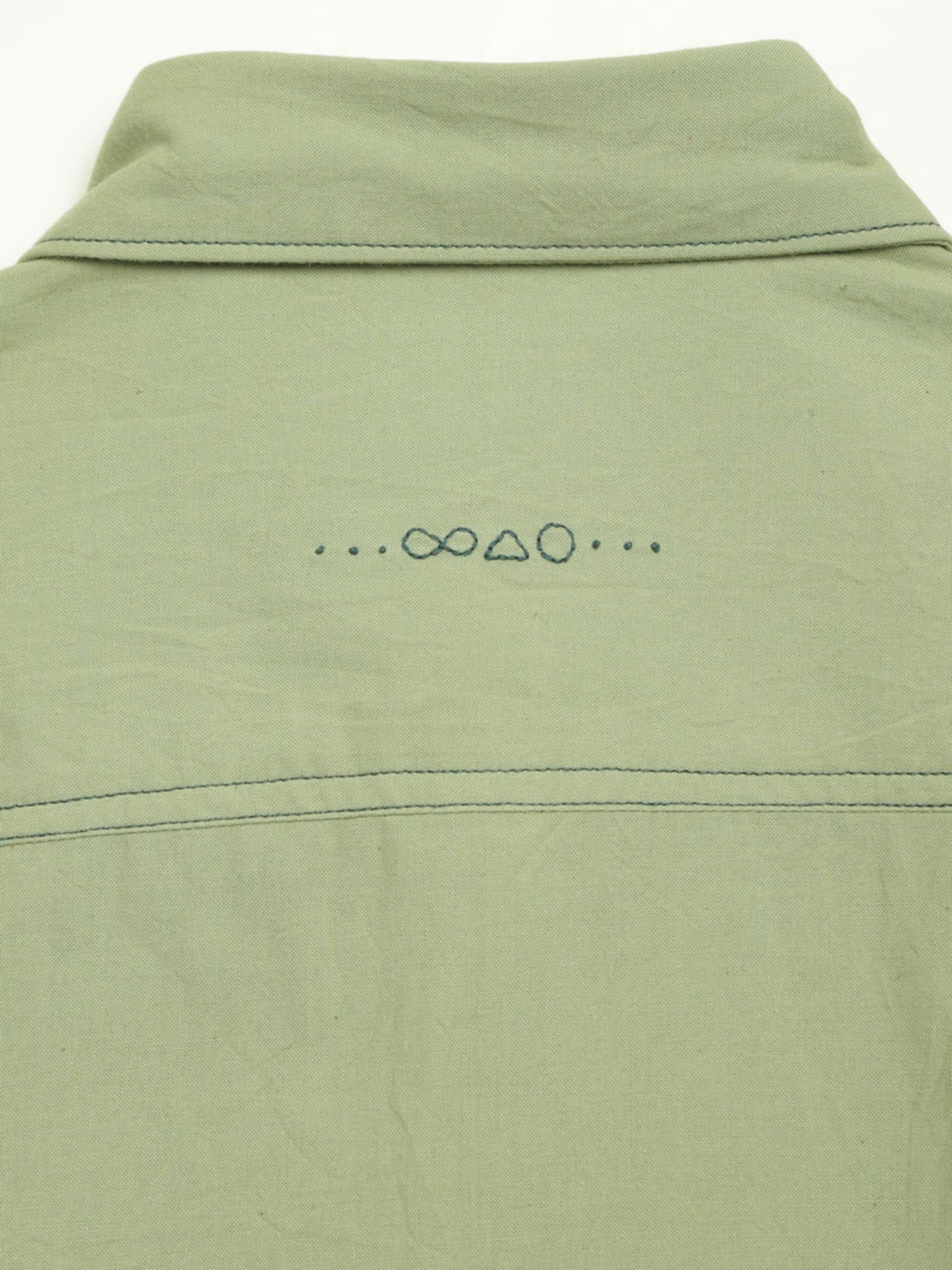 Hand-embroidered symbols on the back yoke of an organic cotton shirt — infinity, triangle and circle motifs in white thread, handcrafted by artisans in Tamil Nadu