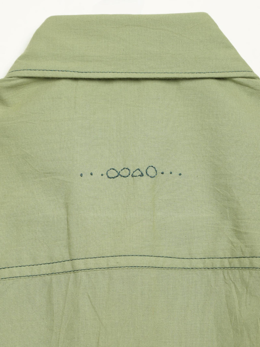 Hand-embroidered symbols on the back yoke of an organic cotton shirt — infinity, triangle and circle motifs in white thread, handcrafted by artisans in Tamil Nadu