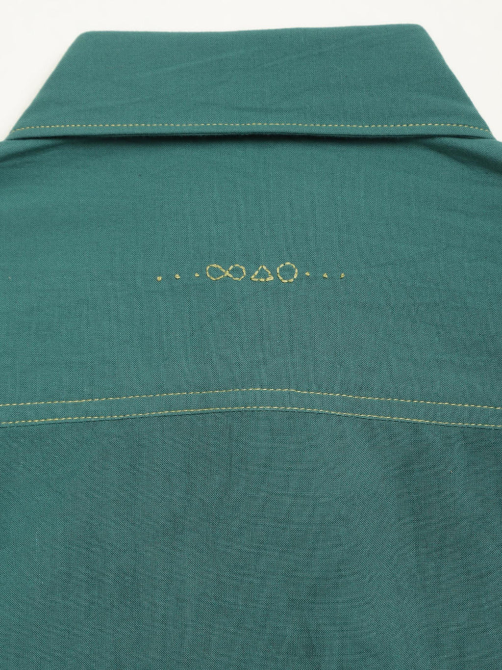 Hand-embroidered symbols on the back yoke of an organic cotton shirt — infinity, triangle and circle motifs in white thread, handcrafted by artisans in Tamil Nadu