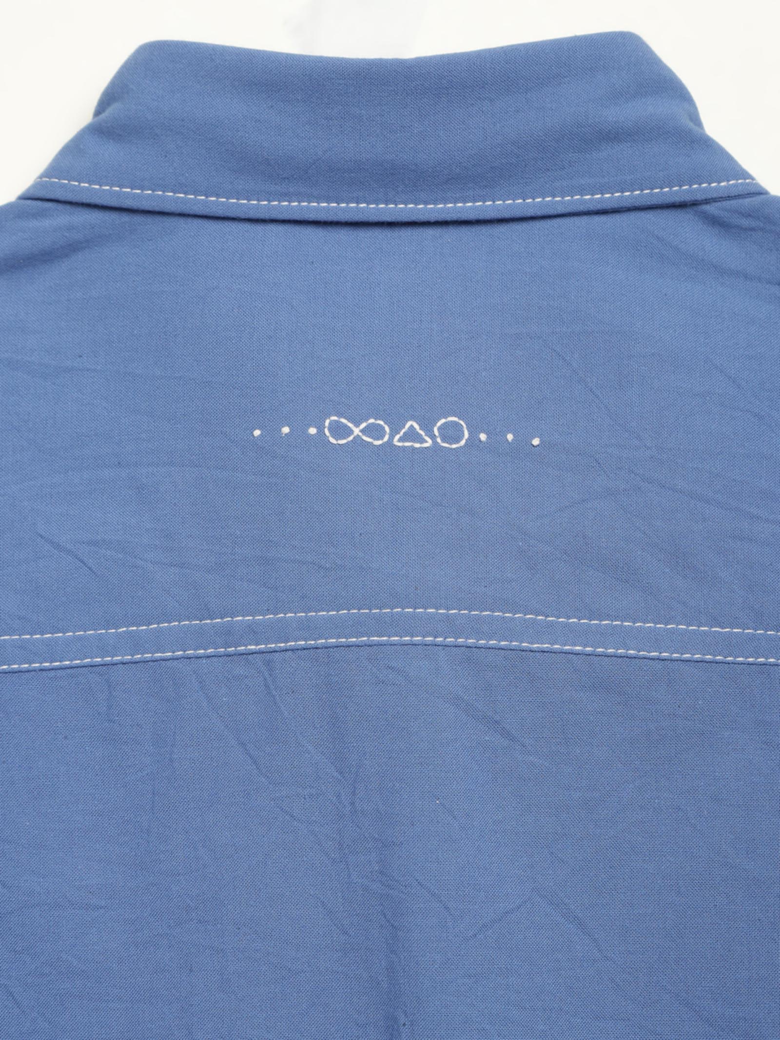 Hand-embroidered symbols on the back yoke of an organic cotton shirt — infinity, triangle and circle motifs in white thread, handcrafted by artisans in Tamil Nadu