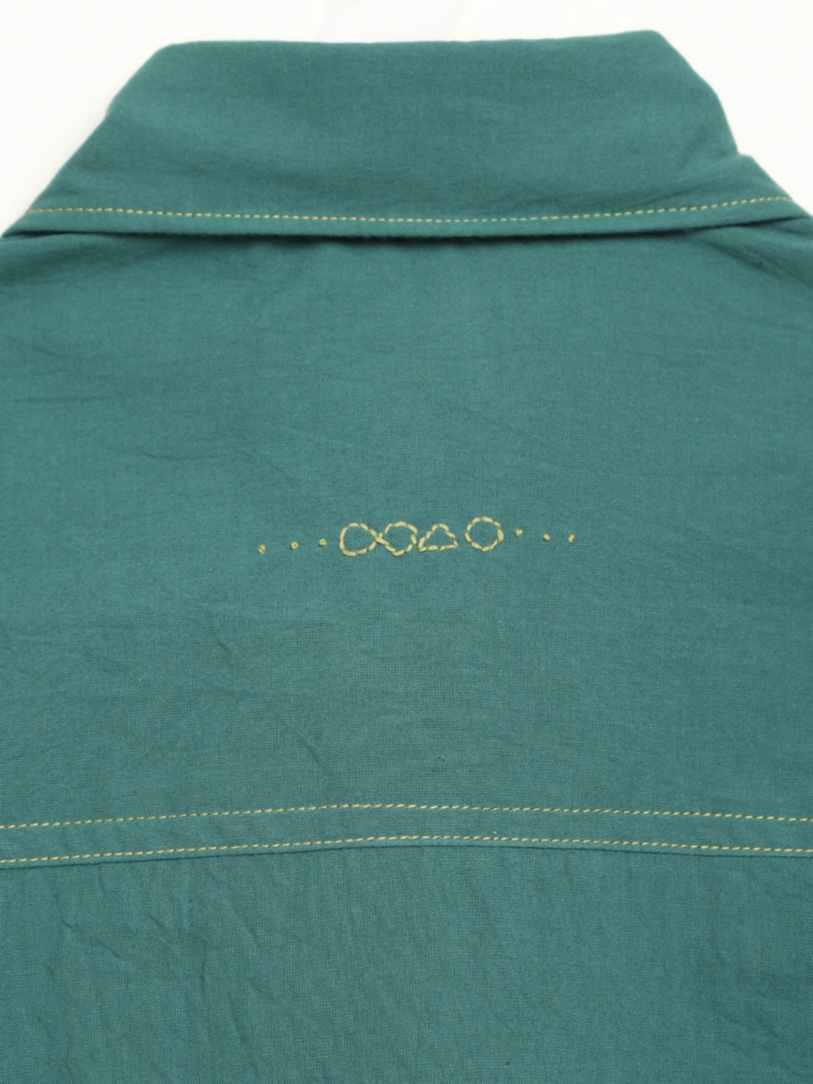Hand-embroidered symbols on the back yoke of an organic cotton shirt — infinity, triangle and circle motifs in white thread, handcrafted by artisans in Tamil Nadu