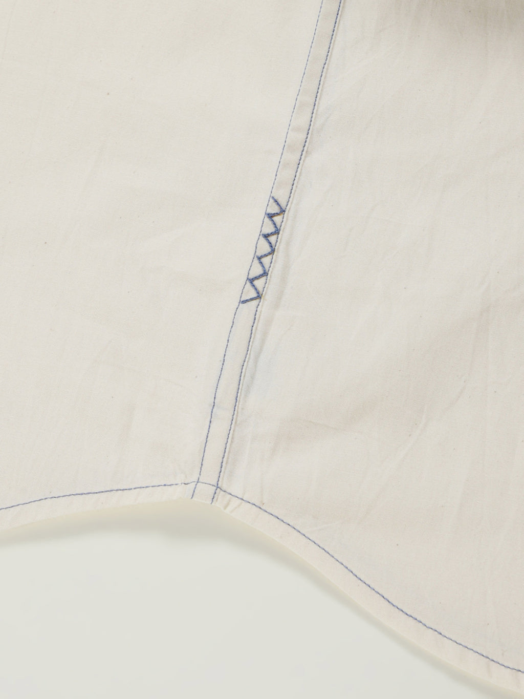 Hand-embroidered zigzag stitch at the side seam hem of a naturally dyed organic cotton shirt, handcrafted by artisans in Tamil Nadu