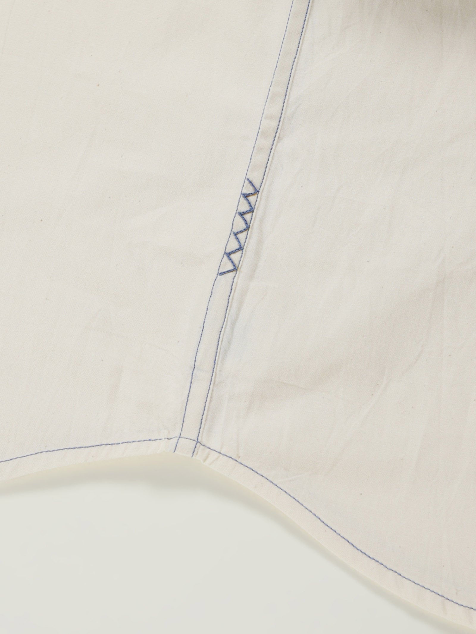 Hand-embroidered zigzag stitch at the side seam hem of a naturally dyed organic cotton shirt, handcrafted by artisans in Tamil Nadu