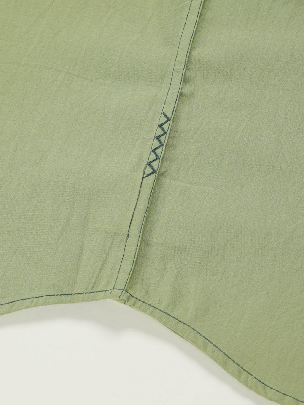 Hand-embroidered zigzag stitch at the side seam hem of a naturally dyed organic cotton shirt, handcrafted by artisans in Tamil Nadu