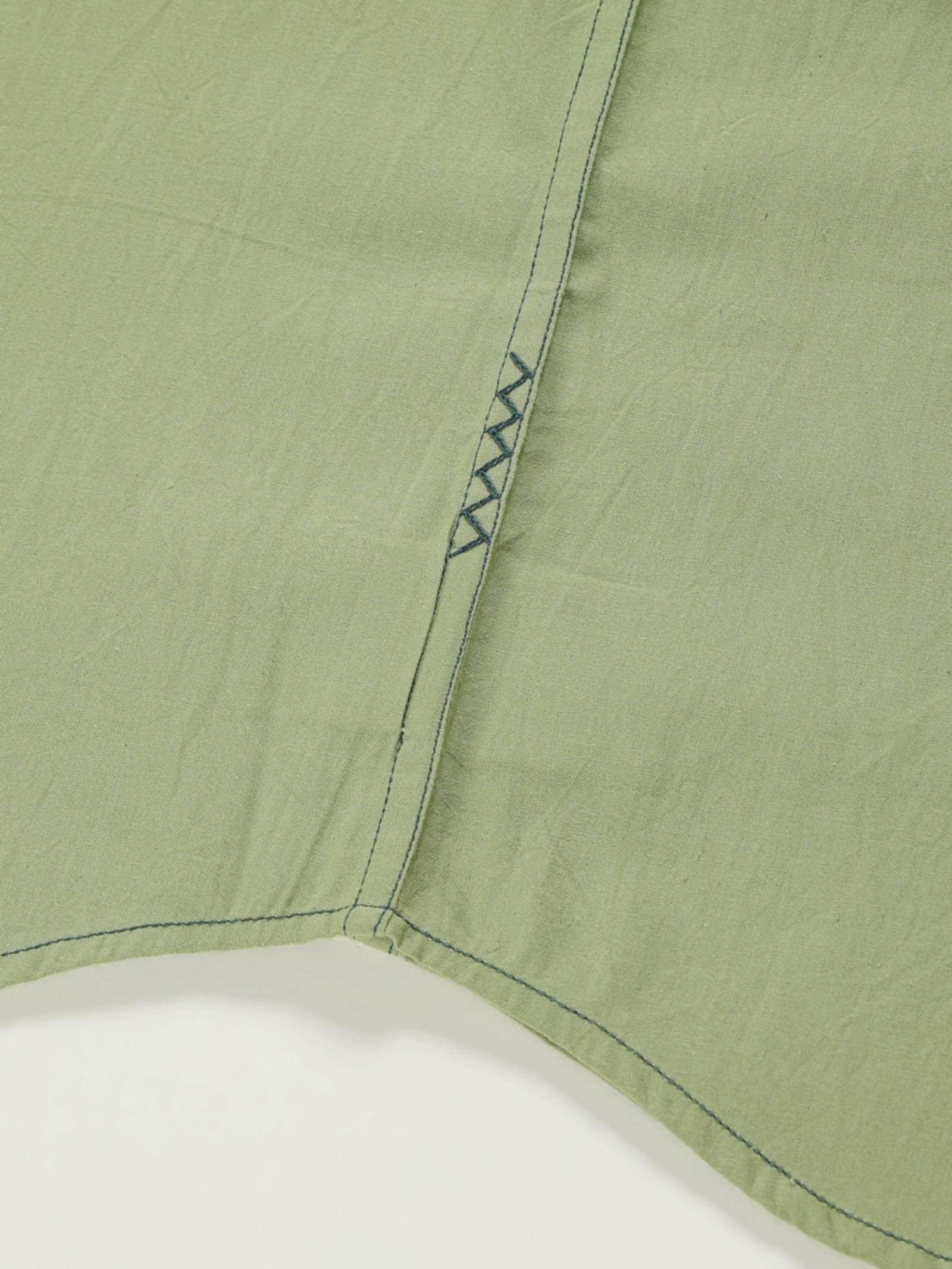 Hand-embroidered zigzag stitch at the side seam hem of a naturally dyed organic cotton shirt, handcrafted by artisans in Tamil Nadu