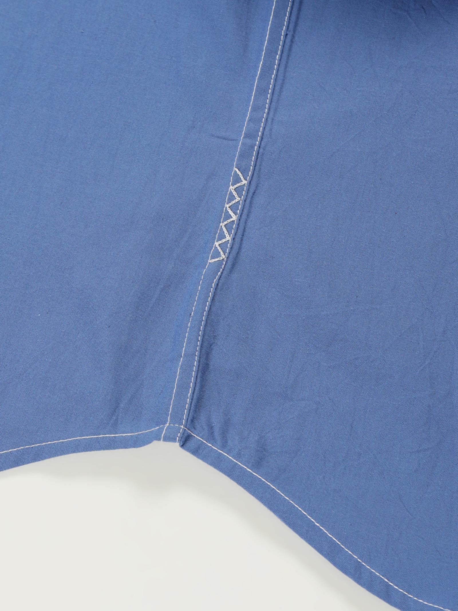 Hand-embroidered zigzag stitch at the side seam hem of a naturally dyed organic cotton shirt, handcrafted by artisans in Tamil Nadu