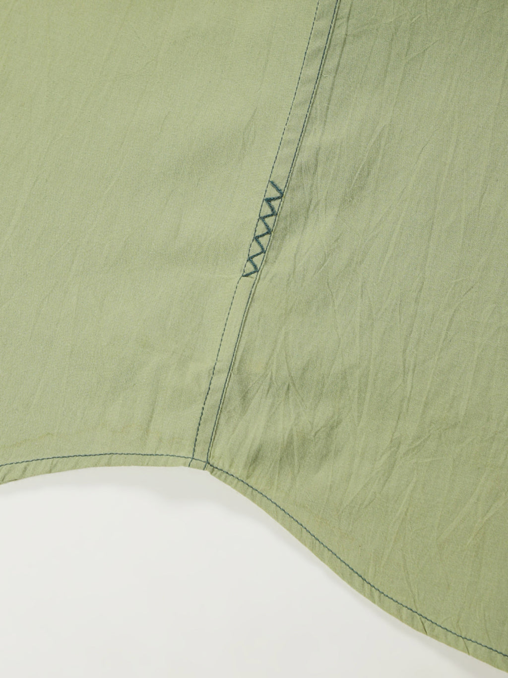 Hand-embroidered zigzag stitch at the side seam hem of a naturally dyed organic cotton shirt, handcrafted by artisans in Tamil Nadu
