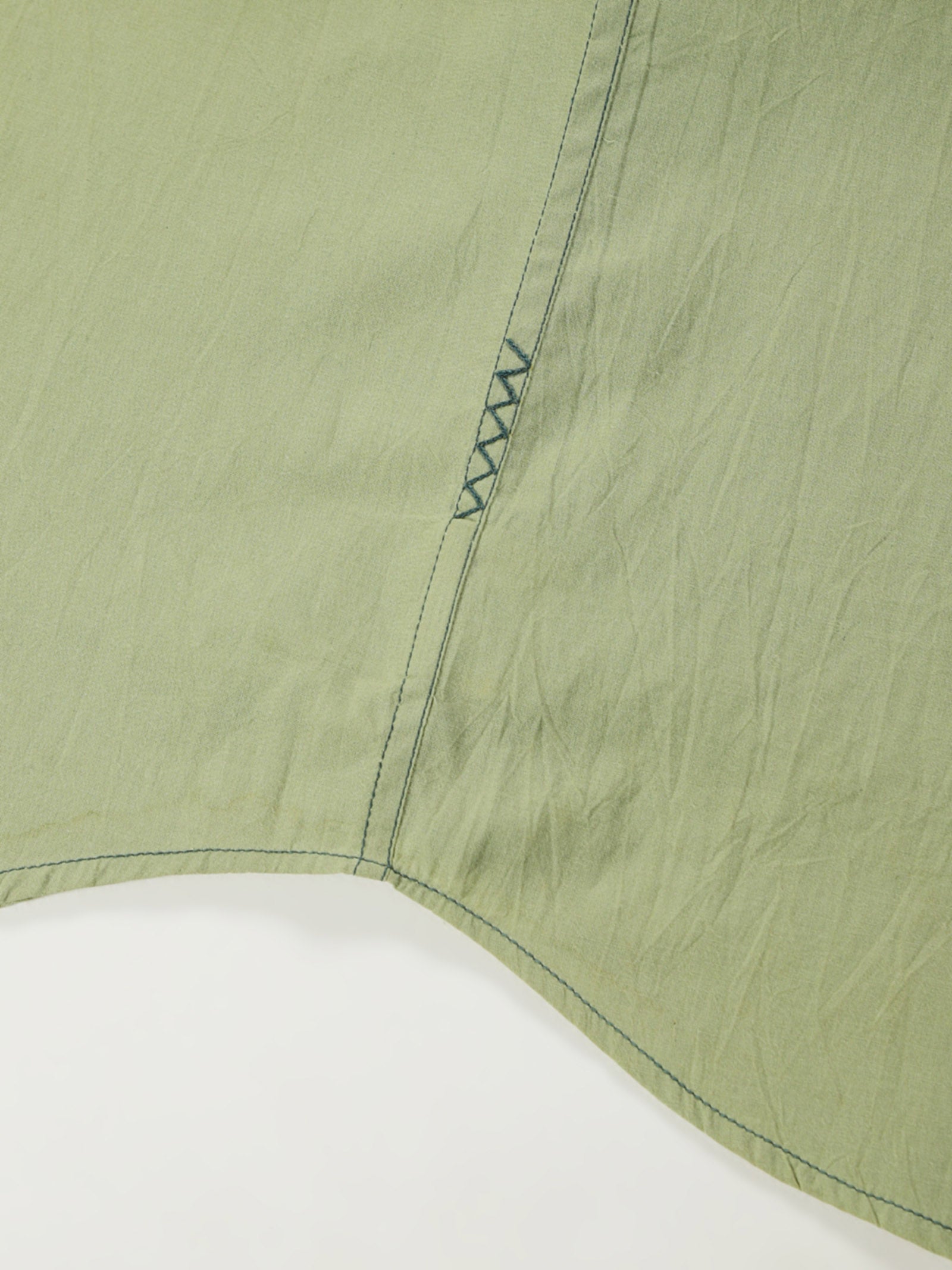 Hand-embroidered zigzag stitch at the side seam hem of a naturally dyed organic cotton shirt, handcrafted by artisans in Tamil Nadu