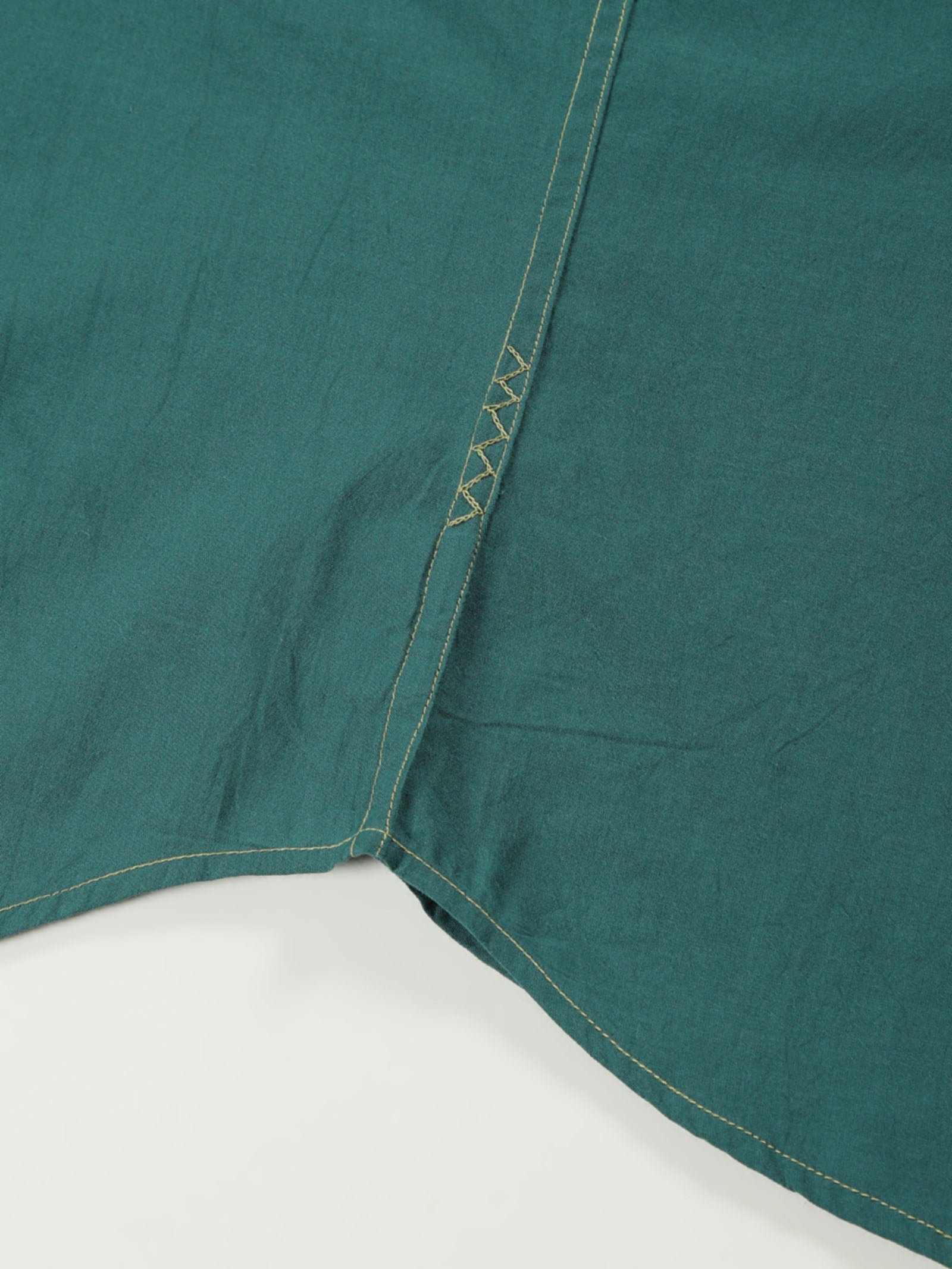 Hand-embroidered zigzag stitch at the side seam hem of a naturally dyed organic cotton shirt, handcrafted by artisans in Tamil Nadu