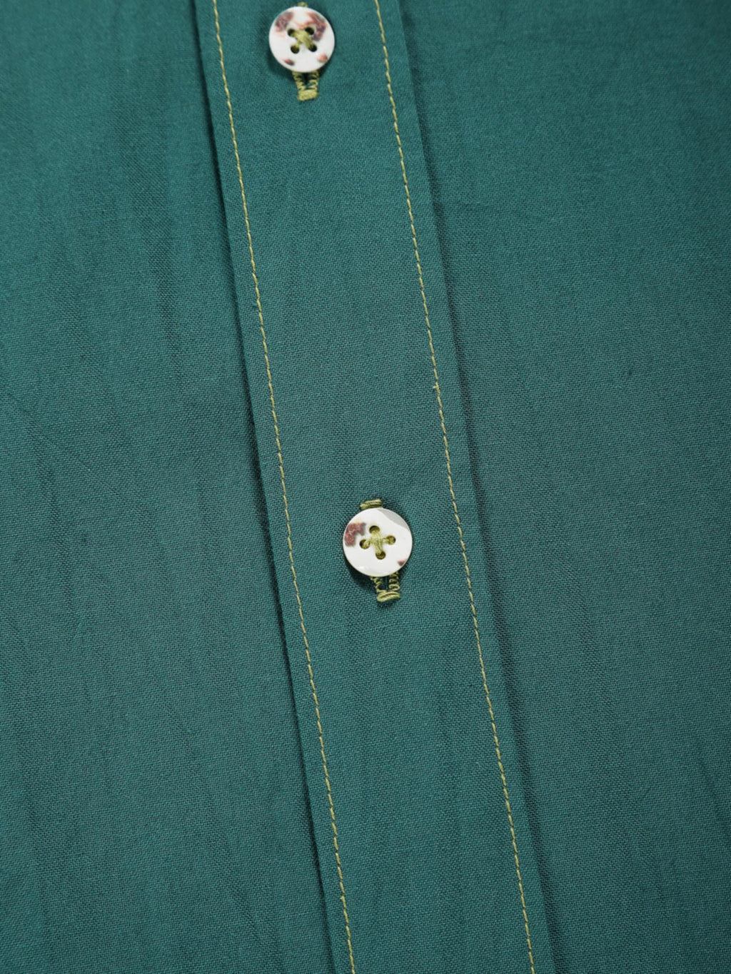 Close-up of old forest plant-dyed organic cotton shirt placket with natural shell buttons and contrast stitching.