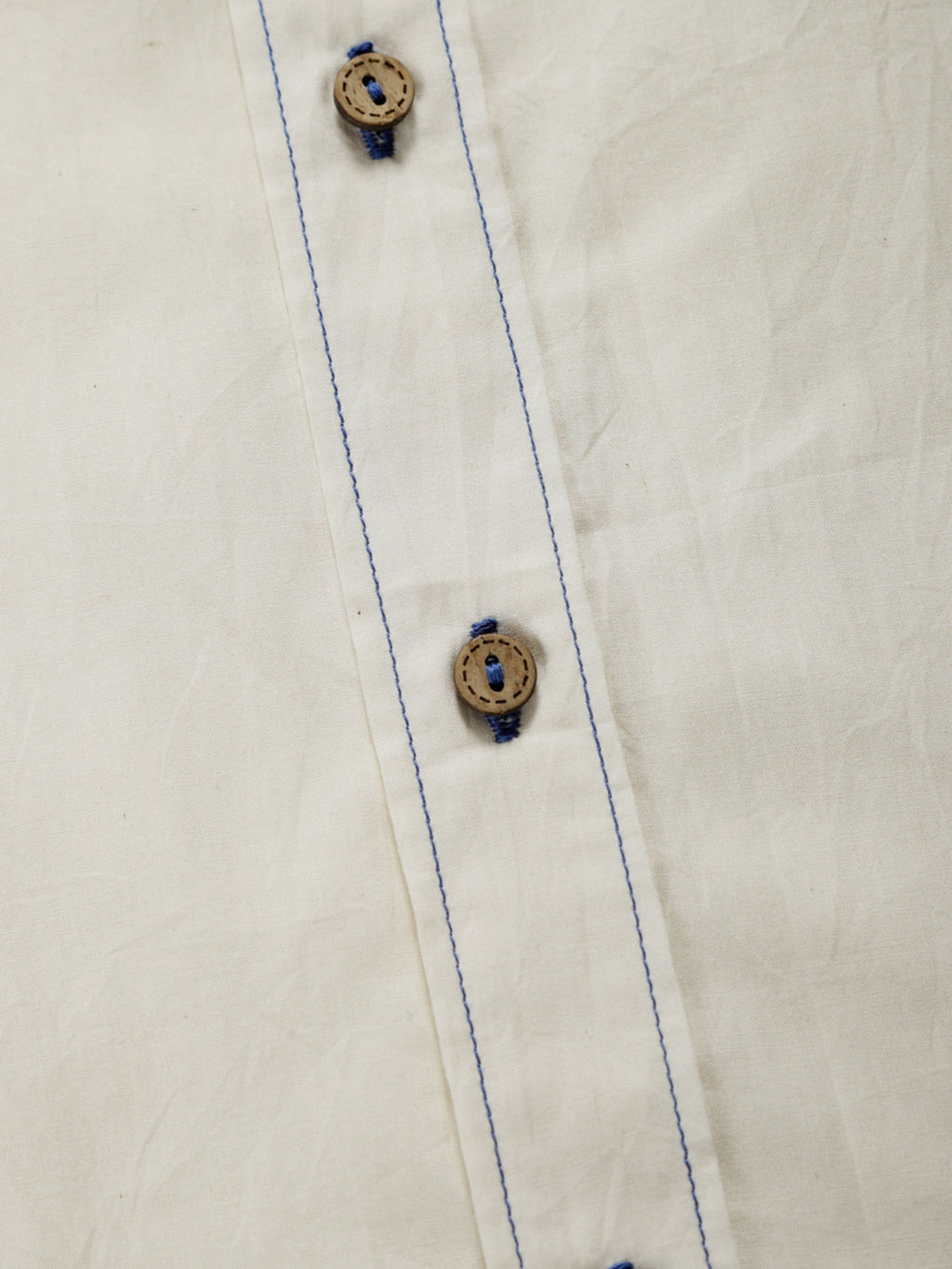 Close-up of undyed organic cotton shirt placket with natural shell buttons and contrast stitching.