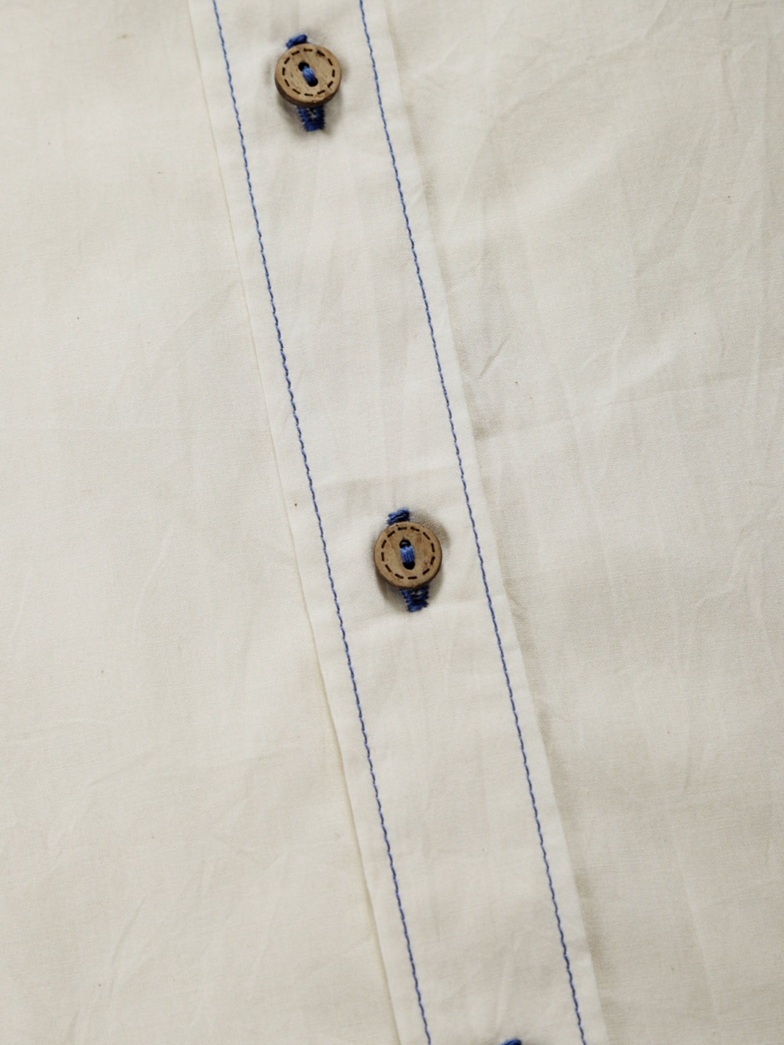 Close-up of undyed organic cotton shirt placket with natural shell buttons and contrast stitching.