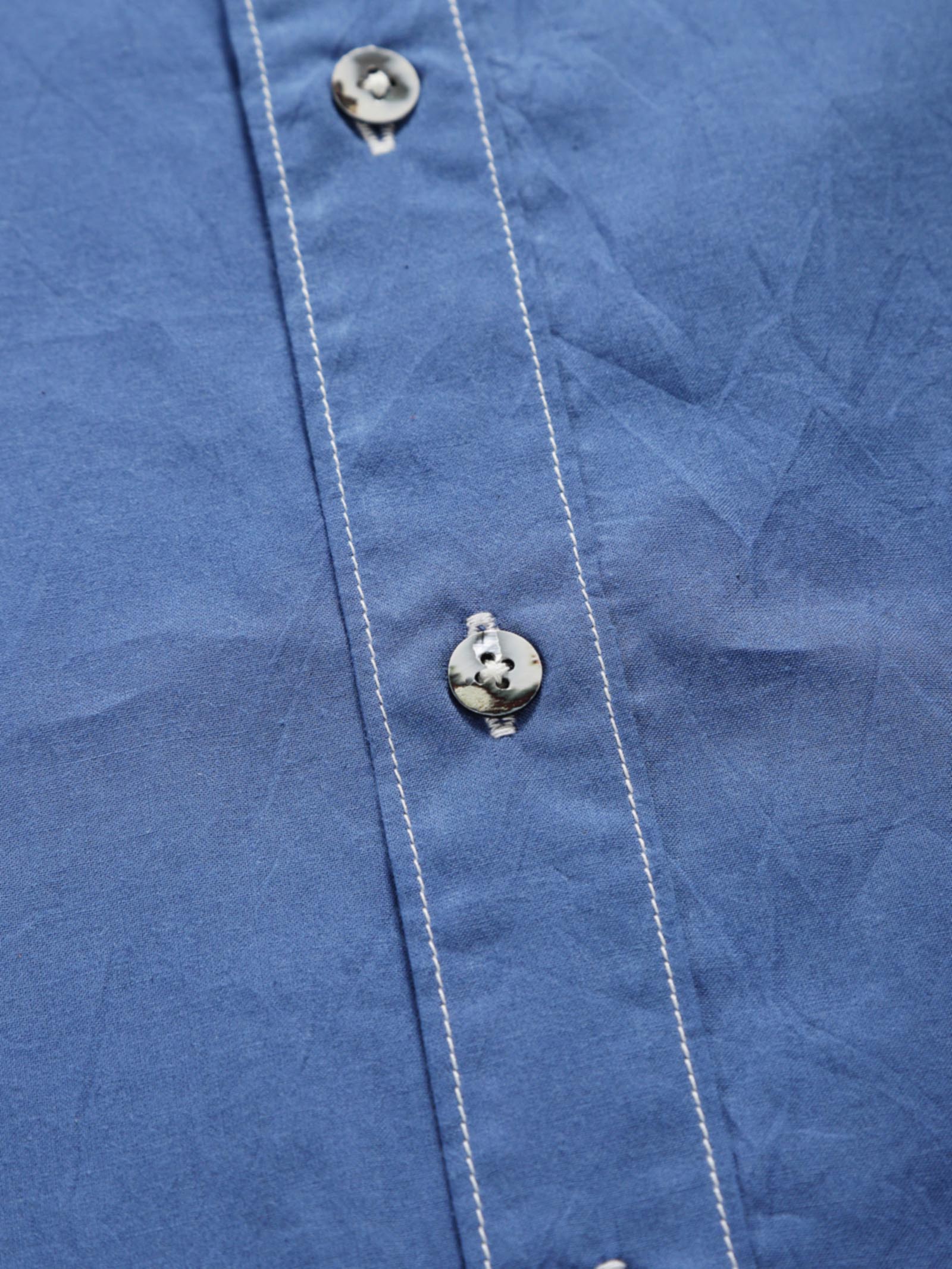 Close-up of quiet blue plant-dyed organic cotton shirt placket with natural shell buttons and contrast stitching.