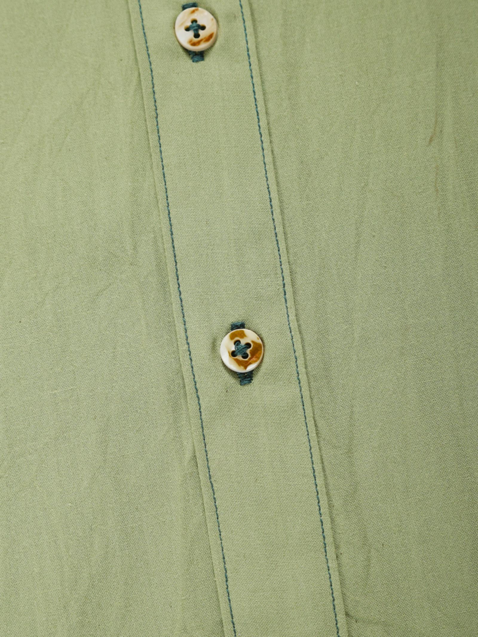Close-up of pale olive plant-dyed organic cotton shirt placket with natural shell buttons and contrast stitching.