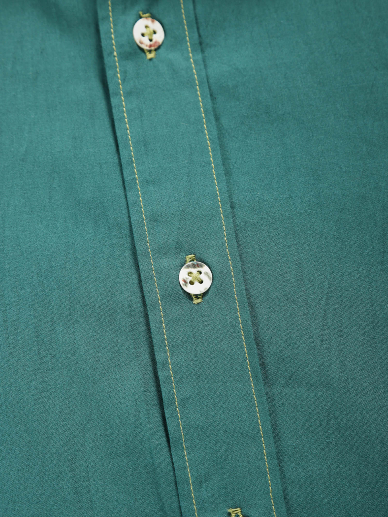 Close-up of old forest plant-dyed organic cotton shirt placket with natural shell buttons and contrast stitching.