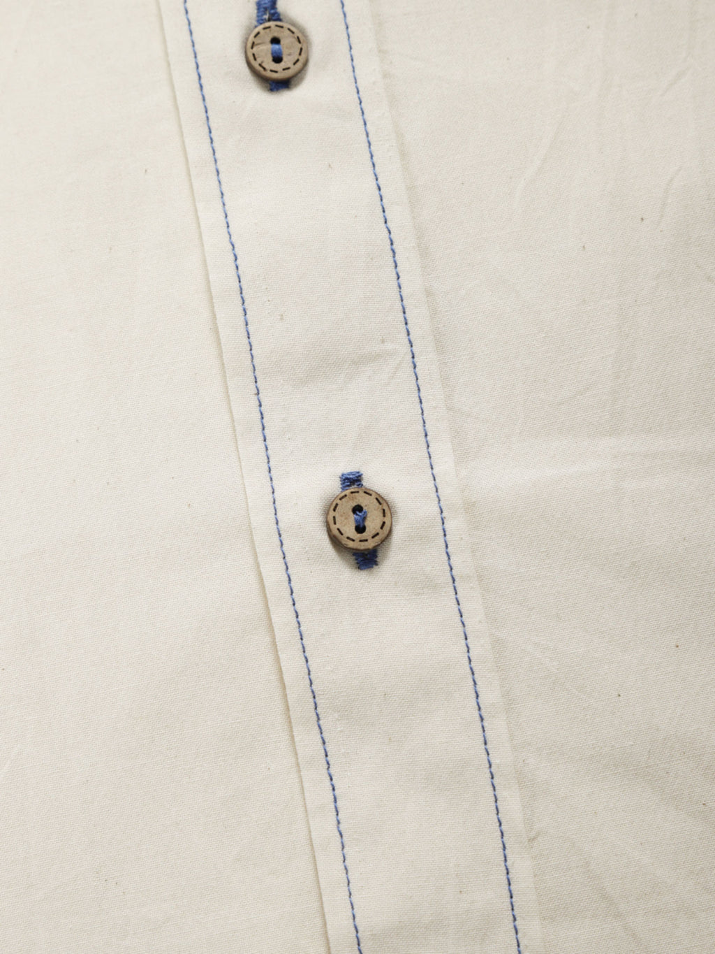 Close-up of undyed organic cotton shirt placket with natural shell buttons and contrast stitching.