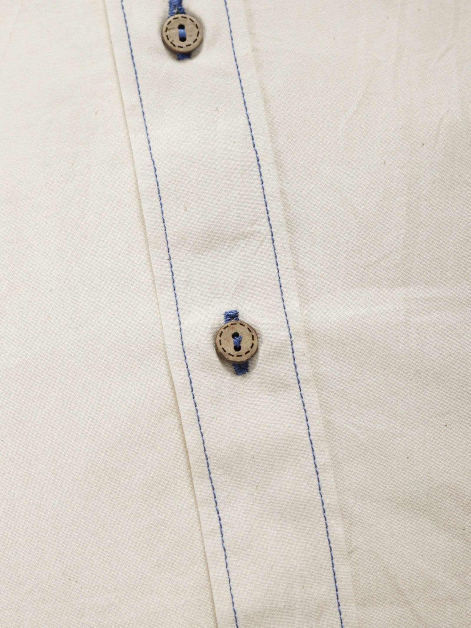 Close-up of undyed organic cotton shirt placket with natural shell buttons and contrast stitching.