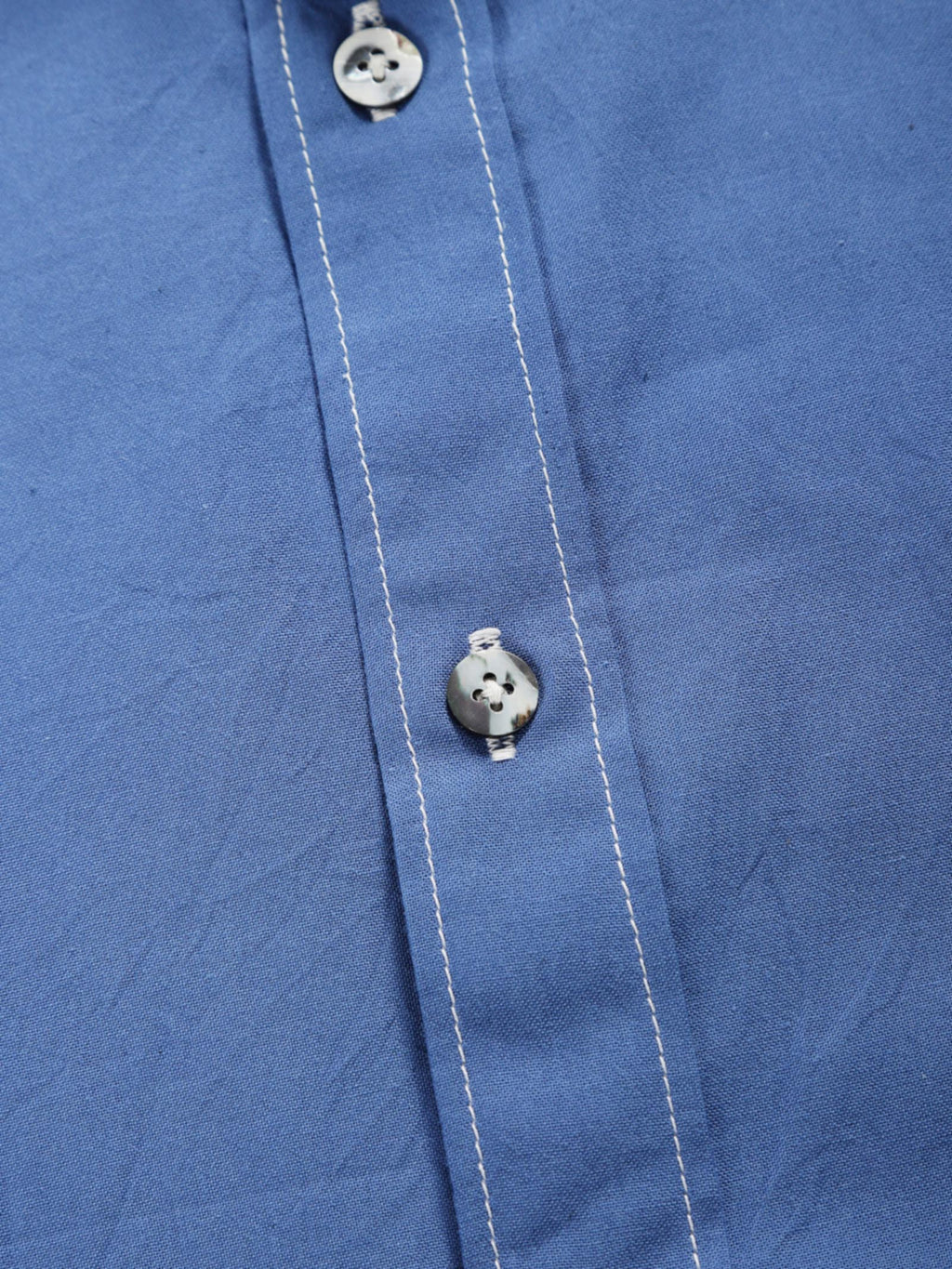 Close-up of quiet blue plant-dyed organic cotton shirt placket with natural shell buttons and contrast stitching