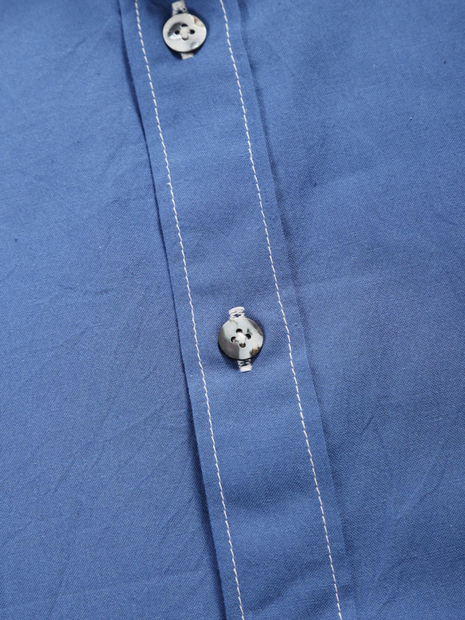 Close-up of quiet blue plant-dyed organic cotton shirt placket with natural shell buttons and contrast stitching