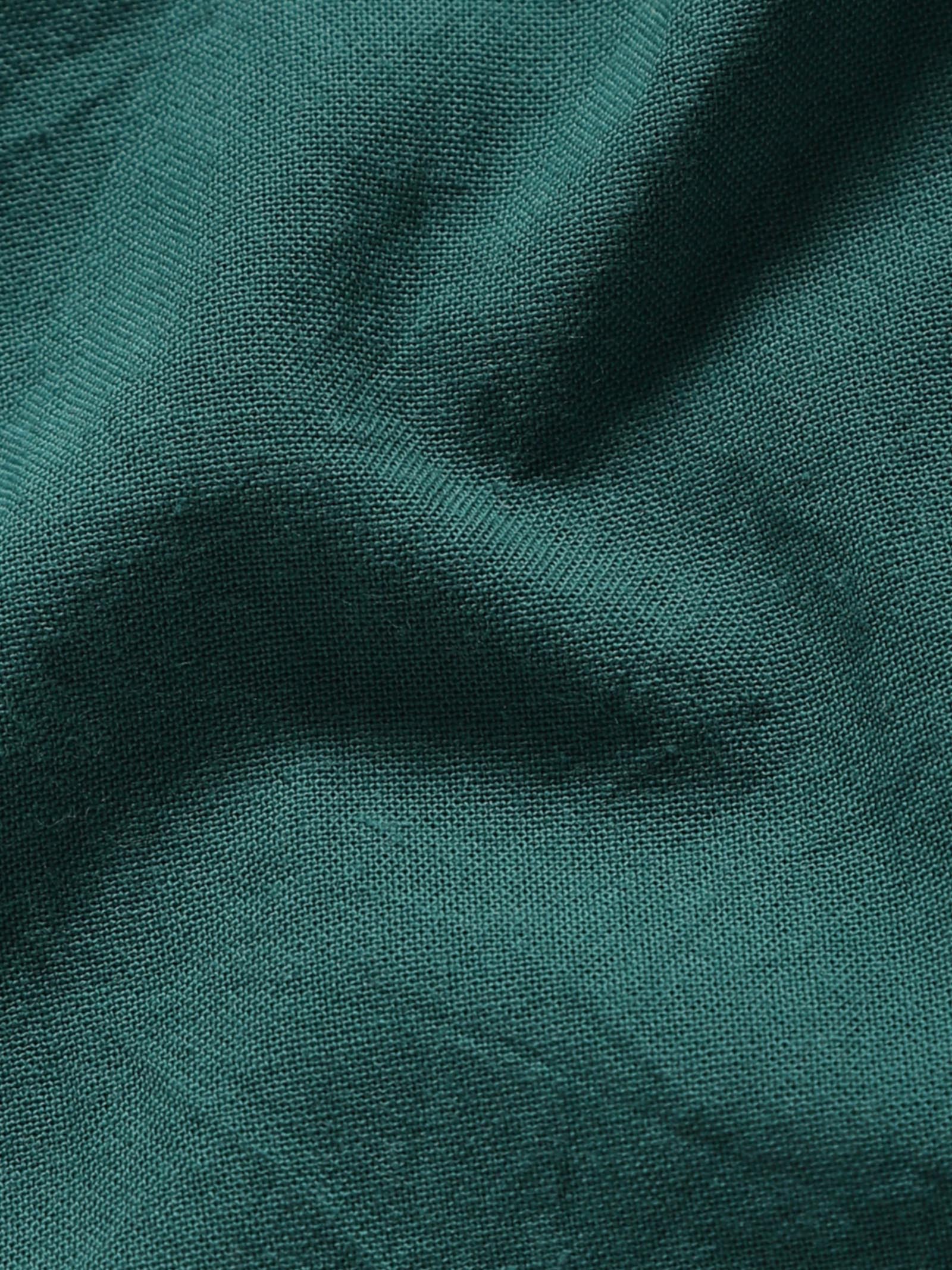 Close-up of pale olive plant-dyed organic cotton fabric showing natural texture and weave