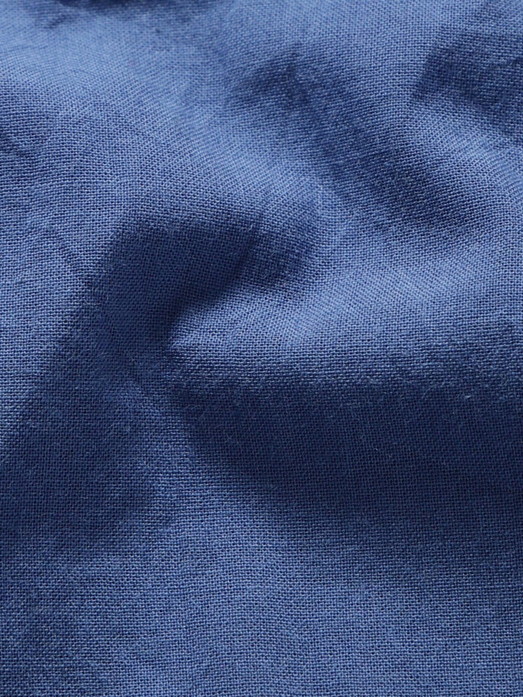 Close-up of pale olive plant-dyed organic cotton fabric showing natural texture and weave.