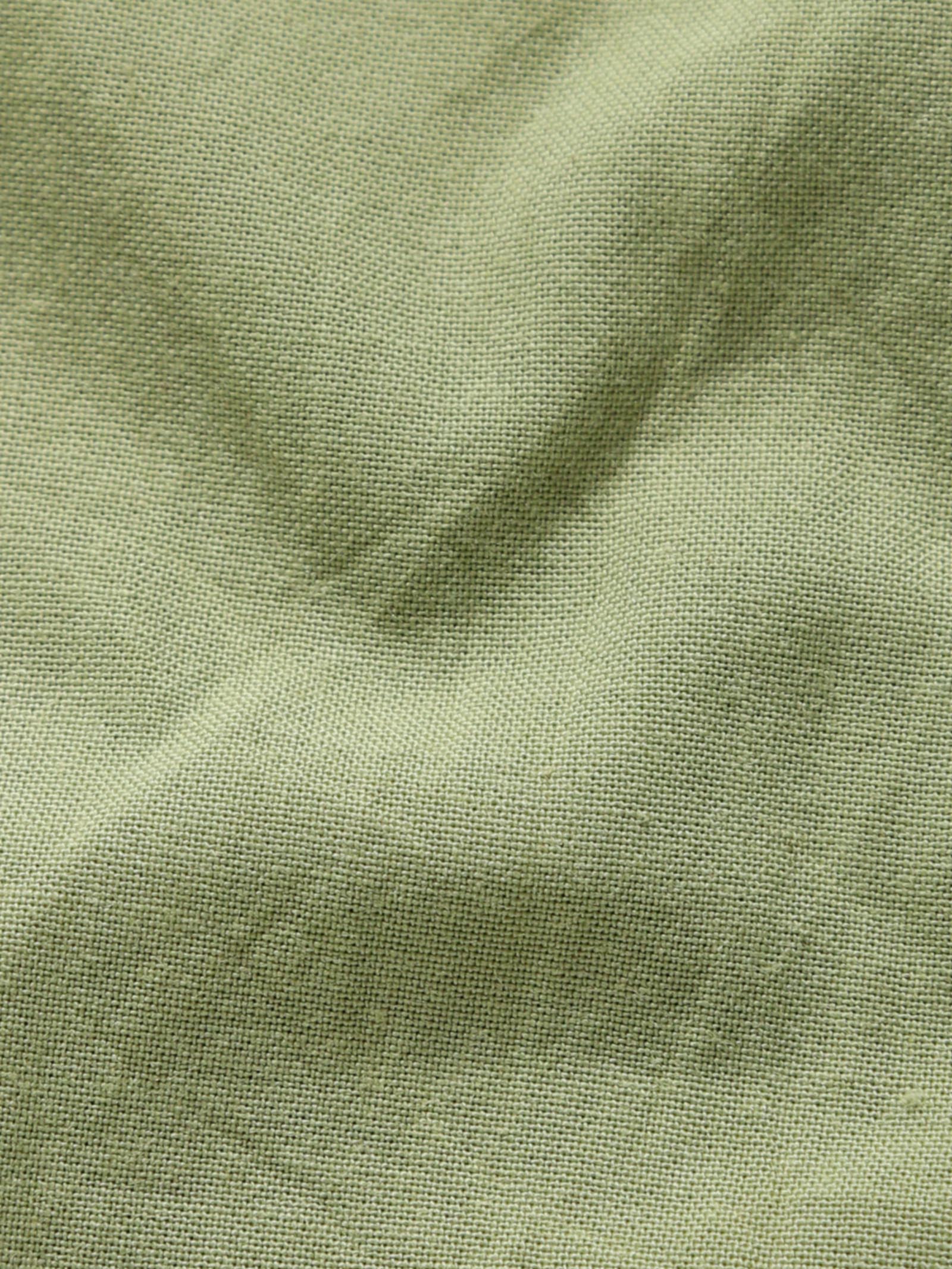 Close-up of pale olive plant-dyed organic cotton fabric showing natural texture and weave.