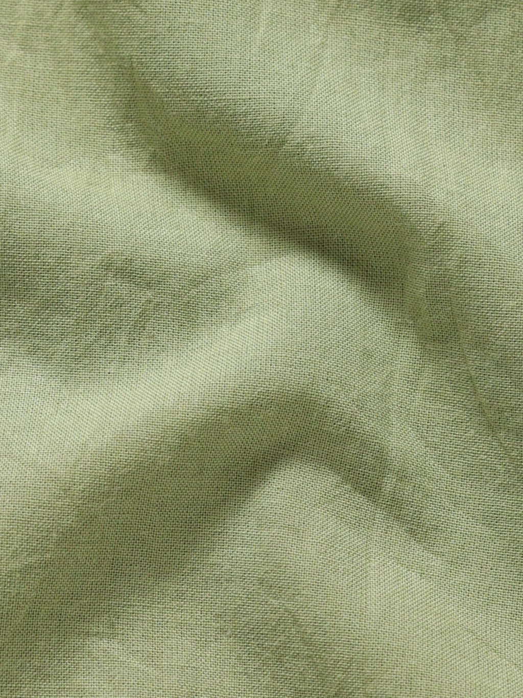Close-up of pale olive plant-dyed organic cotton fabric showing natural texture and weave.