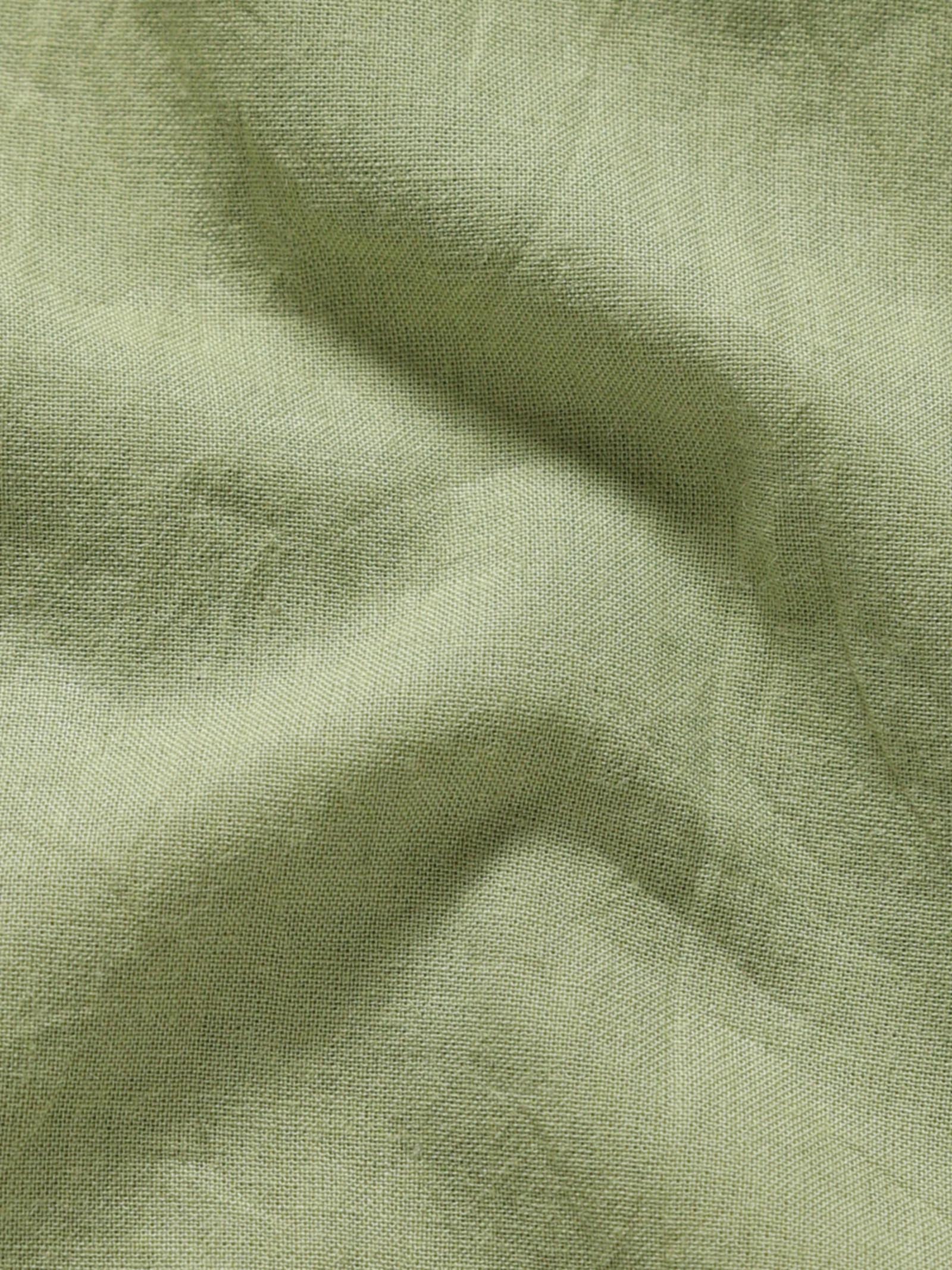 Close-up of pale olive plant-dyed organic cotton fabric showing natural texture and weave.